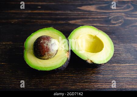 Halved Haas Avocado on a Dark Wood Background: Haas avocado cut in half with the pit still in one piece Stock Photo