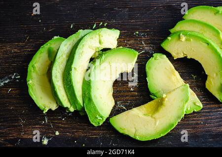 Peeled and Sliced Haas Avocado on a Dark Wood Background: Slices of Haas avocado on a wooden cutting board Stock Photo