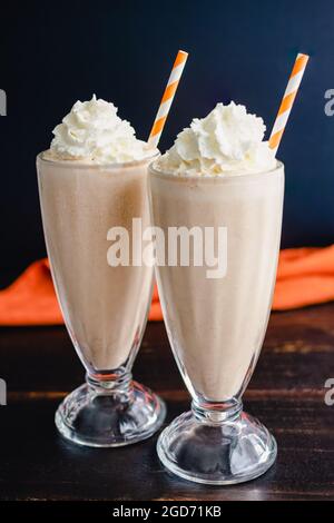 Pumpkin Pie Milkshakes Topped with Whipped Cream: Pumpkin spice milkshakes served in fountain glasses with paper straws Stock Photo