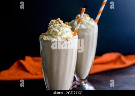 Pumpkin Pie Milkshakes Topped with Whipped Cream and Graham Crackers: Pumpkin spice milkshakes served in fountain glasses with paper straws Stock Photo