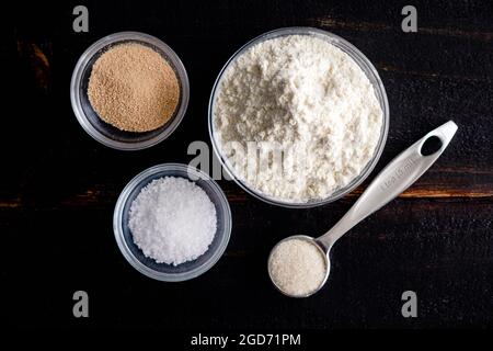 French Bread Ingredients on a Wood Table: Flour, yeast, sugar, and salt in a dark wood background Stock Photo