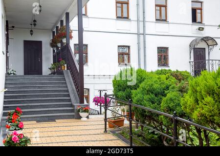 flowerpots with flowers at staircase of front porch with ceiling lantern of white building faced with granite stone with wooden railings the exterior Stock Photo