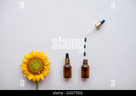 Flat lay of sunflowers and sunflower seeds and bottles for cosmetic serum or cream on a light pink background. The concept of beauty and preservation Stock Photo