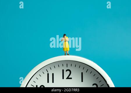 Miniature people toy figure photography. Reading routine concept. A girl student standing read a book above clock. Image photo Stock Photo