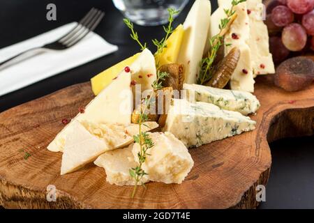 Cheese plate served with grapes, jam, figs, crackers and walnuts on a dark stone background Stock Photo