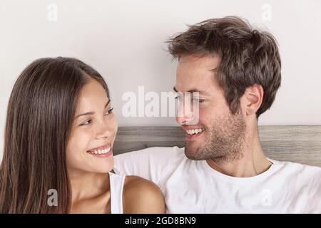 Happy couple in love smiling at each other looking into their eyes portrait at home of interracial relationship Asian woman, Caucasian man Stock Photo