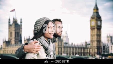 Happy couple by Big Ben Parliament, River Thames, London. Romantic young couple enjoying view during travel. Asian woman, Caucasian man in London Stock Photo