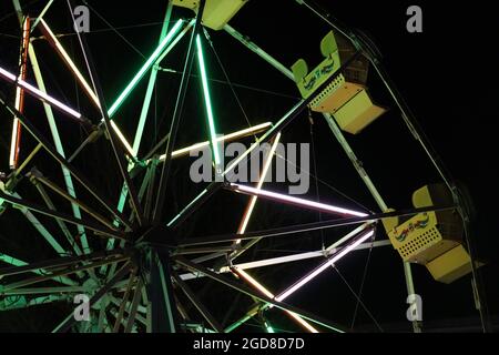 Ferris Wheel with Yellow Seats and Green Lighting, against a Pitch Black Night Sky Stock Photo