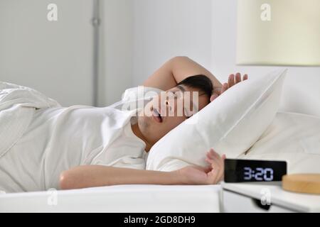 Young Asian man sleeping and snoring loudly lying in the bed Stock Photo