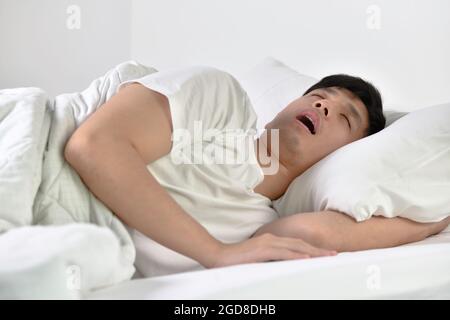 Young Asian man sleeping and snoring loudly lying in the bed Stock Photo