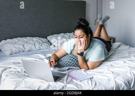 Curvy latin woman lying on bed using computer in Latin America, plus size female Stock Photo