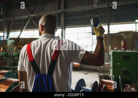 Engineer in uniform using crane controller hanging from ceiling in a factory Stock Photo