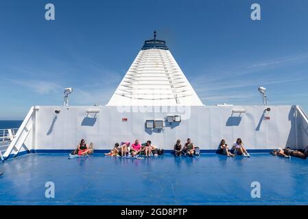 Passengers sunbathing on the deck of a car ferry in front of the funnel, Tyrrhenian Sea, Tuscany, Italy Stock Photo