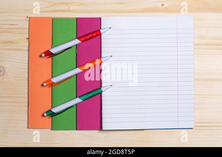 Colored school notebooks and three pens on wooden desk, top view. Space for text Stock Photo