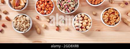 Many different nuts in bowls on a wooden table, healthy vegan snacks panorama Stock Photo