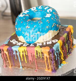A colorful cake featuring a blue donut design on top, with vibrant dripping rainbow icing and the text "Schulkind," celebrating a special occasion. Stock Photo