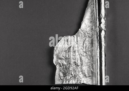 Crumpled foil against a gray background. Roll of aluminum foil for food packaging with an uneven torn edge. Food packaging. Top view. Copy space. Stock Photo
