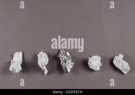 Minimalist composition with crumpled foil and white paper against a gray background. Pieces of aluminum foil and paper in a row. Top view. Copy space. Stock Photo