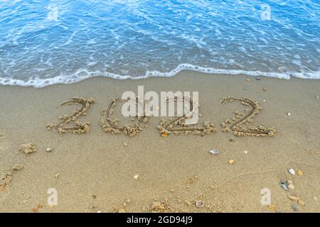 The numbers 2022 are written in the sand. New year on the beach. Sea coast, wave. Place for your text. Summer in winter. Vacation on the ocean. Copy Stock Photo