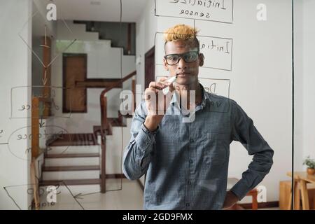 Serious young software developer drawing general flow chart on glass wall in office of IT company Stock Photo