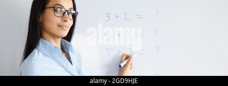 Woman teacher standing at blackboard with formulas and explaining information Stock Photo