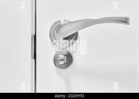 Metallic doorknob and bolt on a white wooden door. Detail Stock Photo