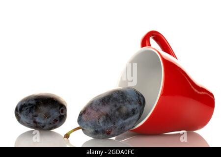 Two ripe organic Damson plums with a red cup, close-up, isolated on white. Stock Photo