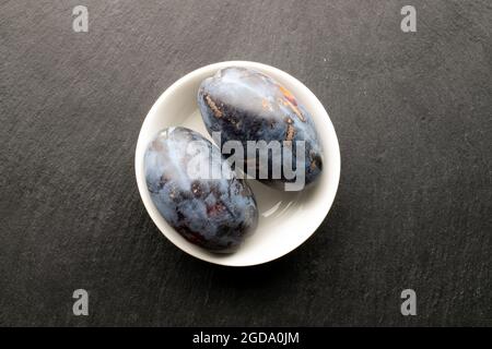 Two juicy dark purple plums, close-up, on a slate serving board, top view. Stock Photo