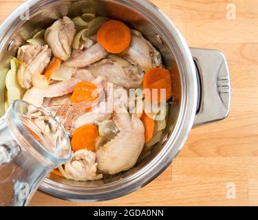 Pours water into the pan with vegetables and meat. Stock Photo