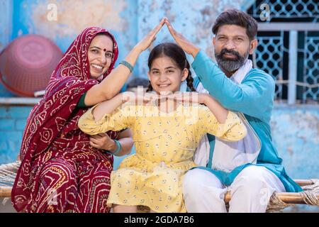 Portrait of smiling Happy rural indian family forming house roof with their hands at village home, Parents care for child protection, Father and mothe Stock Photo