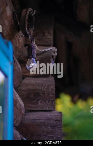 Switched-off light bulb hangs on a wooden house close-up with copy space Stock Photo