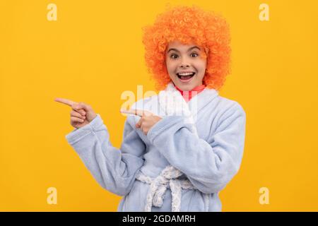 amazed girl with orange hair in cozy sleepwear. pointing finger on copy space. Stock Photo