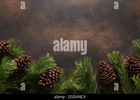Christmas border with evergreen branches and cones on brown background. New Year. Top view. Xmas holiday greeting card. Copy space. Stock Photo