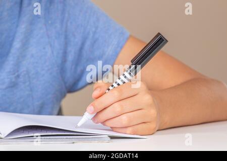Boy hand holding pen in left hand and writing in a notebook, doing homework. Left Handers Day Stock Photo