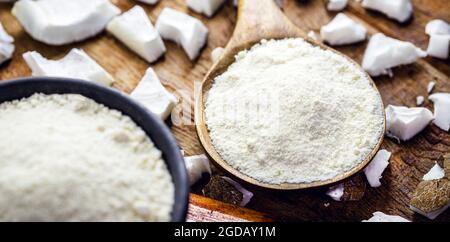 full rustic wooden spoon and coconut flour, on wooden table with coconut in the background, culinary ingredient. Stock Photo