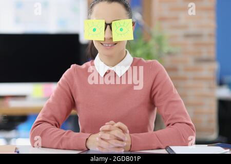 Young woman sitting at table with stickers pasted on glasses Stock Photo
