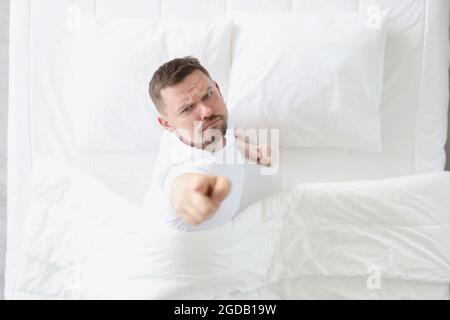 Young man lying in white bed and showing index finger up top view Stock Photo