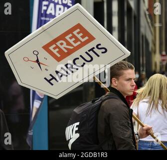 Manchester, UK, 12th August, 2021. Daily life on the streets of city centre Manchester, UK. A young man carries a wooden 'free haircuts' sign in city centre Manchester, UK, directing people to a hairstyling or barber shop where people train to become hairstylists.   Credit: Terry Waller/Alamy Live News Stock Photo