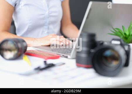 Woman typing on laptop keyboard at table with camera lenses closeup Stock Photo