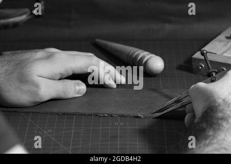 Grayscale closeup of a man's hands working with a tool for leather crafting. Stock Photo