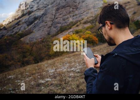 caucasian bearded man traveling in the wild nature using smartphone, with backpack, autumn style, traveler and adventure, free spirit. copy space. Stock Photo