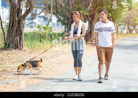 People couple walking with friendly pet beagle dog modern family morning activity for healthy. Stock Photo