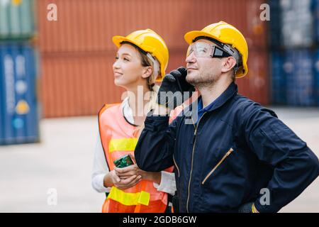 logistic worker teamwork working using smartphone calling command order control loading containers at port cargo to trucks for export and import goods Stock Photo