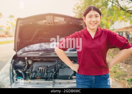 Portrait Happy women standing front of broken accidents car open hood smiling waiting car insurance at roadside with no worry. Stock Photo