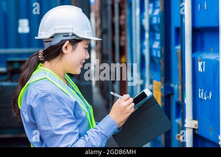Happy woman worker working in port shipping for cargo logistic checking and manage import export goods containers using tablet. Stock Photo