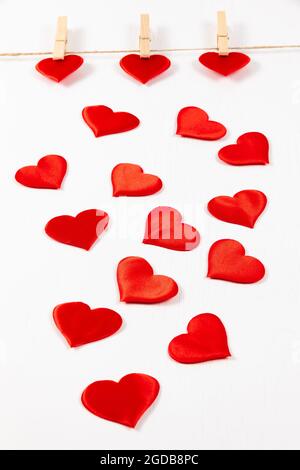 three wooden clothespins hang on a rope on a white background and hold a heart. many hearts scattered. selective focus Stock Photo