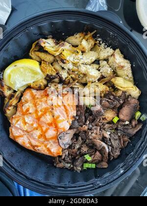 Grilled Salmon Lunch with grilled artichokes and sautéed mushrooms in black plastic bowl Stock Photo