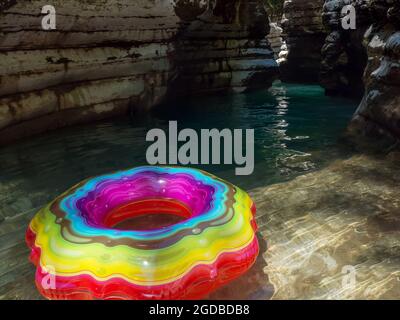 Swimming ring with multicolored pattern on clear turquoise water in a shady canyon gorge Stock Photo