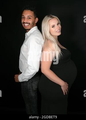 Profile view of a stylish and happy multi-ethnic couple expecting a baby in a back-to-back pose Stock Photo