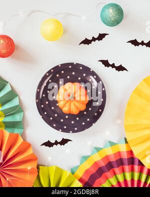 Helloween, autumn composition with small pumpkin on a plate, colorful paper fans, helloween decorations and light garland on a blue background. Cute, Stock Photo
